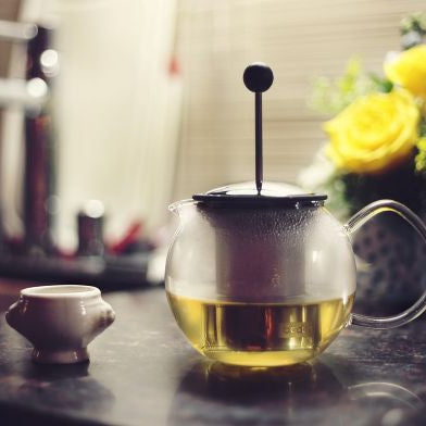 Teapot with tea and a small cup on a table with a blurred background
