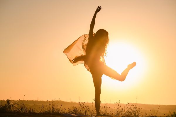 Person dancing in a field with the sun setting in the background